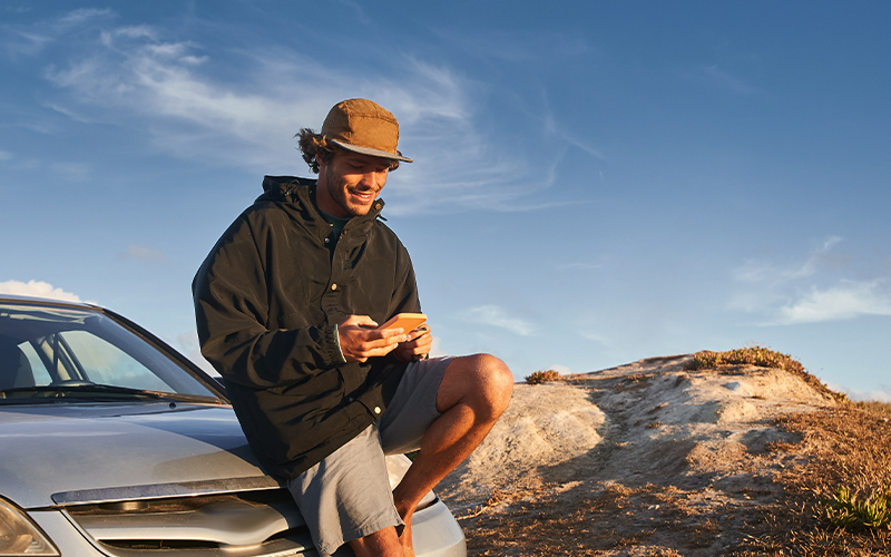 A man sitting on the hood of a car looking at his phone